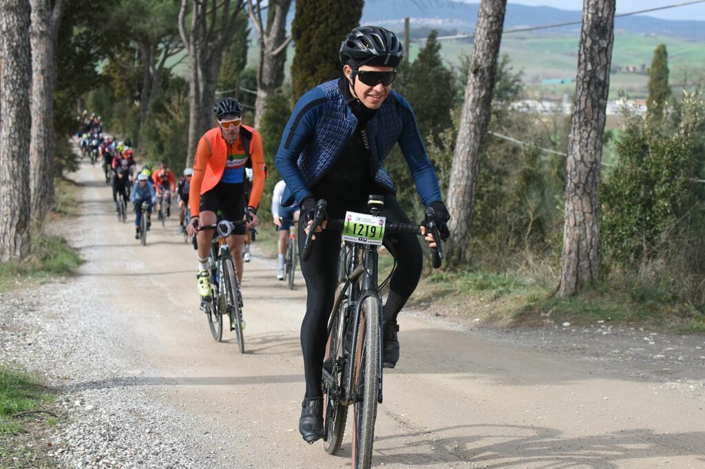 Avanzando por un tramo de tierra blanca, rodeados de viñedos toledanos bajo un cielo azul claro en el Gran Fondo Strade Bianche.